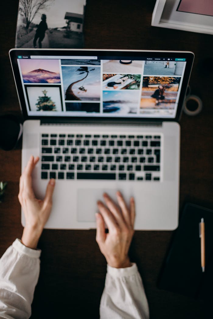 Hands using a laptop to browse photo galleries, illustrating digital creativity and remote work.